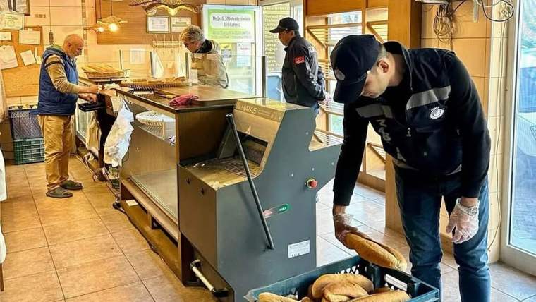 İç mekânda bir kişi kasaya ekmek dizerken, arkada üç kişi tezgâh ve ürünlerle ilgileniyor.