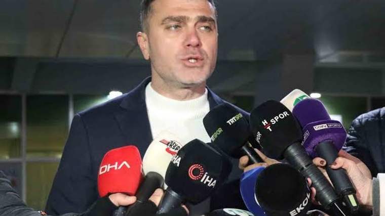Bir kişi, mikrofonlarla çevrili olarak basın mensuplarına açıklama yapıyor.