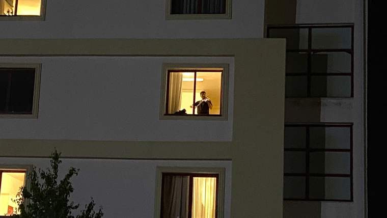 Gece aydınlatılmış apartmanın penceresinde, elinde keman ve yay bulunan bir kişi görülüyor.