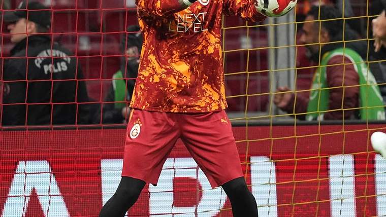 Galatasaray armalı forması ve eldivenleri görülen kaleci, kale önünde topu elleriyle tutuyor.