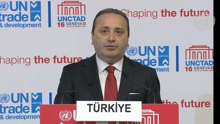 Kürsüde konuşan bir kişi, önündeki TÜRKİYE yazılı tabelanın arkasında duruyor.