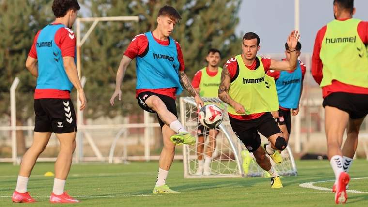 Çim sahada beş futbolcu, antrenman sırasında topun çevresinde koşup pas çalışması yapıyor.
