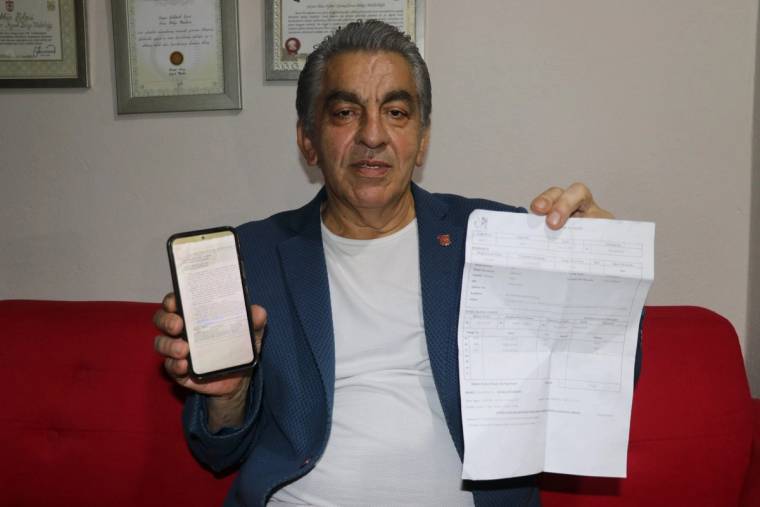 Bir kişi, elinde akıllı telefon ve üzerinde yazılar bulunan bir belgeyle kırmızı koltukta oturuyor.