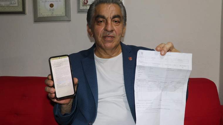 Bir kişi, elinde akıllı telefon ve üzerinde yazılar bulunan bir belgeyle kırmızı koltukta oturuyor.