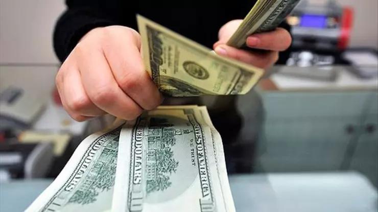Bir kişi, kasada farklı kupürlerde ABD doları banknotlarını elleriyle sayıyor.