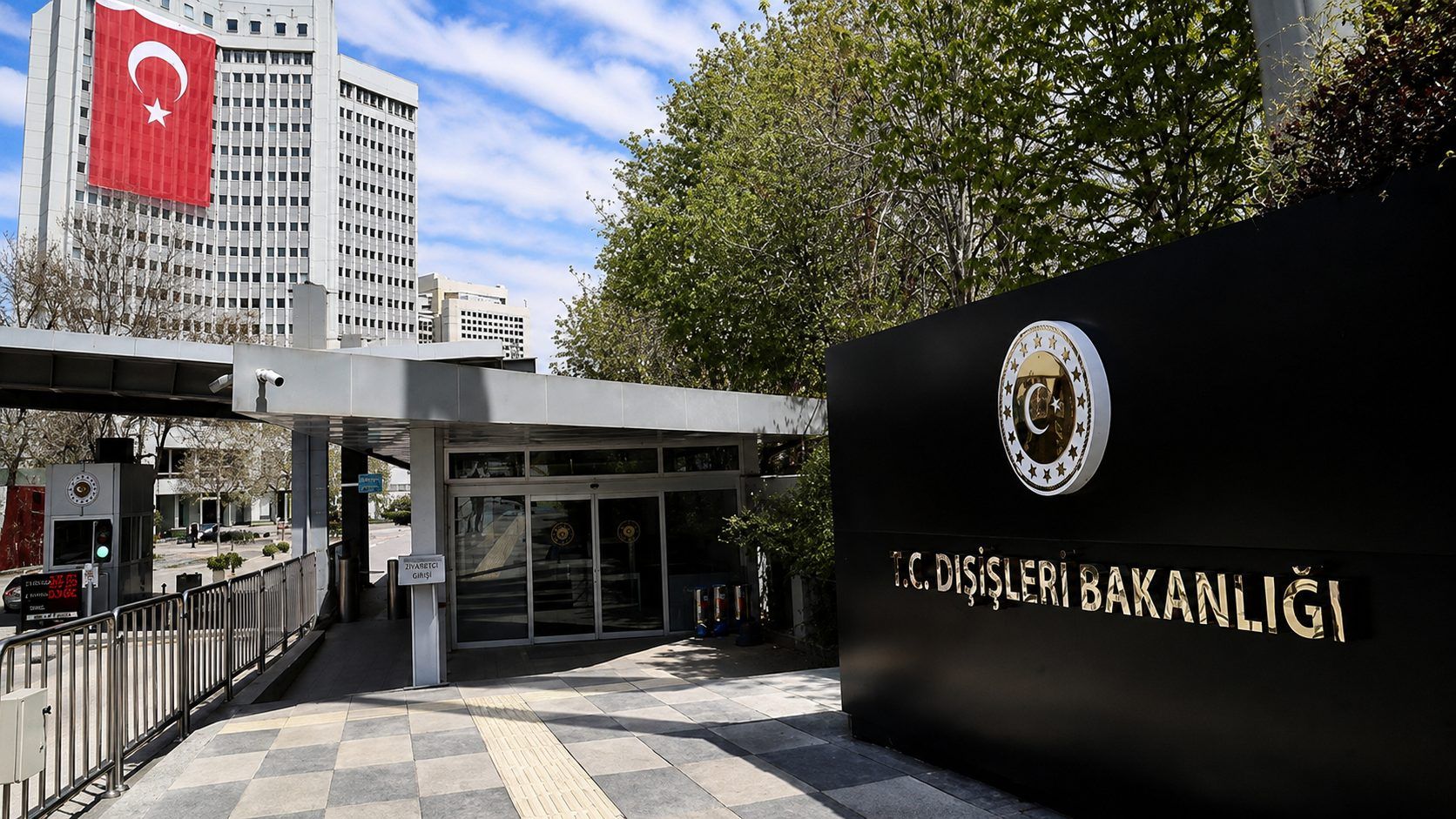 Üzerinde “T.C. Dışişleri Bakanlığı” yazan giriş, yanında Türk bayrağı bulunan yüksek bina ve ağaçlarla çevrili.
