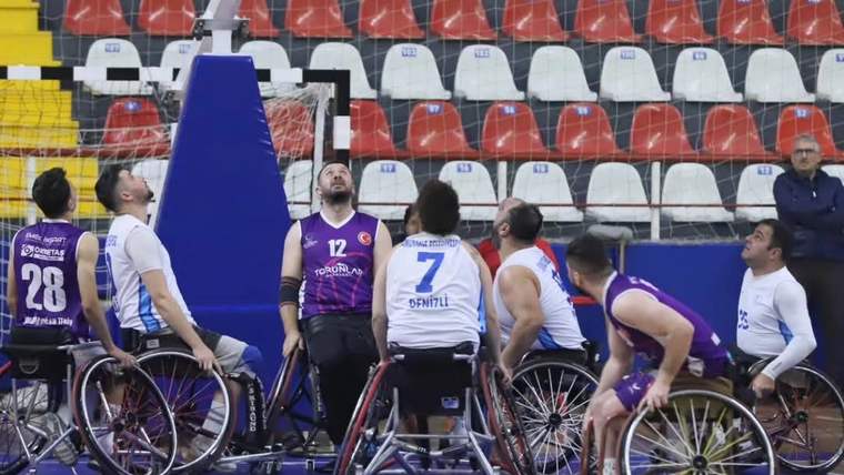 Tekerlekli sandalyede basketbol oynayan sporcular, potaya odaklanmış şekilde bekliyor.