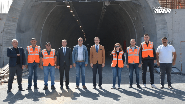 Tünel girişinin önünde, bazıları turuncu iş yeleği giyen dokuz kişi yan yana duruyor.