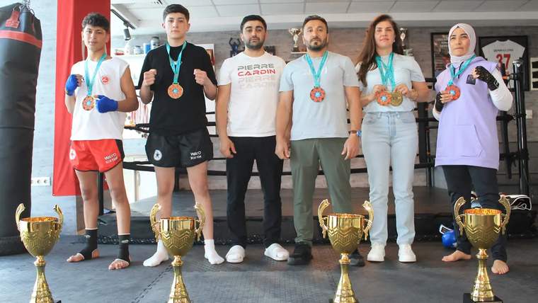 Kick boks takımı, madalyalar ve kupalarla birlikte stüdyoda poz veriyor.