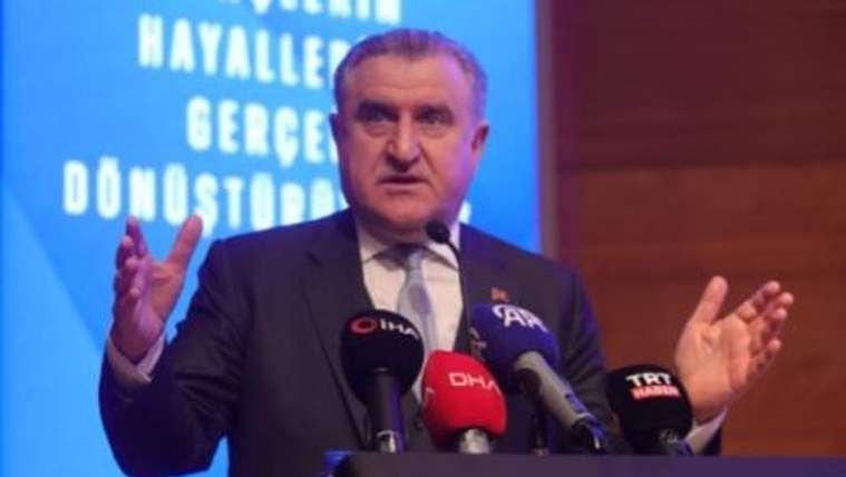 Bir kişi, mikrofonların önünde el hareketleriyle konuşuyor.
