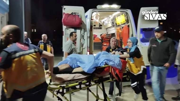 Gece vakti sağlık görevlileri, sedyeyle taşınan yaralı kişiyi ambulansın açık kapısına götürüyor.