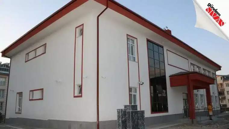 Yeni eğitim yılına hazırlanan beyaz bir okul binası, önünde taş sütunlar var.
