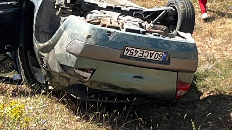 Tavanı üzerine devrilmiş, ağır hasarlı bir otomobil kuru otların arasında duruyor.