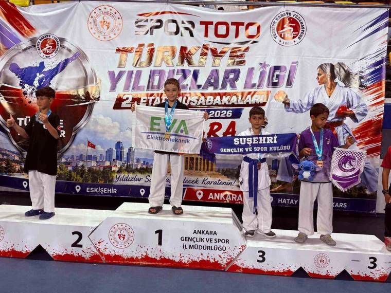 Karate kıyafetli dört çocuk, madalya ve kupalarıyla podyumda; arkalarında turnuva pankartı bulunuyor.