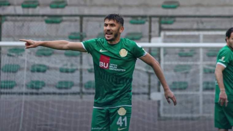 Yeşil forma giymiş bir futbolcu, sahada işaret ederek bir şeyler anlatıyor.