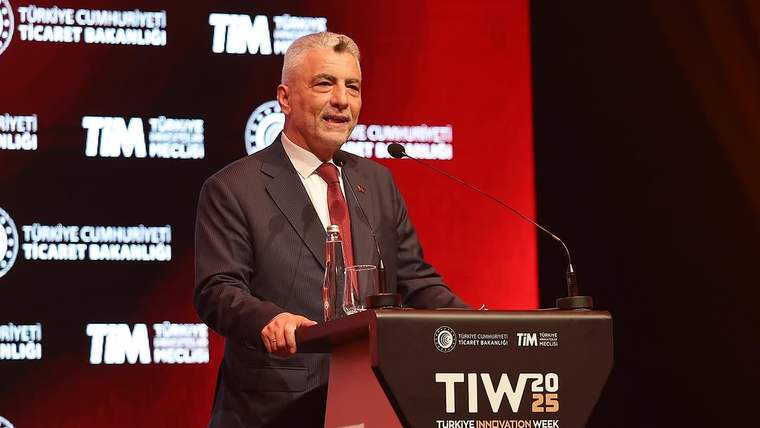 Kürsüde konuşan bir kişi, kırmızı arka plan önünde mikrofon ve su şişesiyle duruyor; kürsüde TİM 2025 yazıyor.