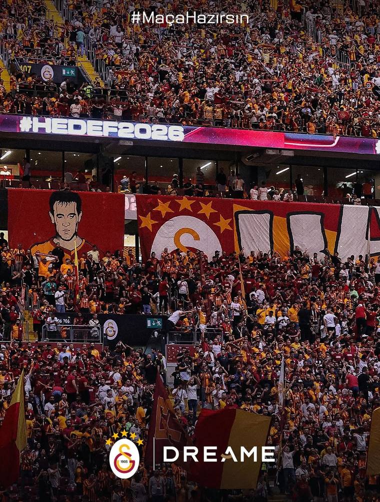 Galatasaray renkleriyle süslenmiş tribünlerde çok sayıda taraftar, bayraklar ve büyük takım flamaları görülüyor.
