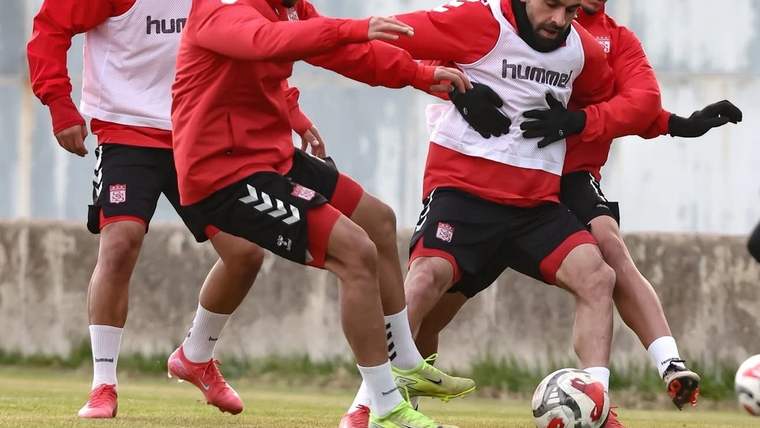 Kırmızı-beyaz formalar giyen dört futbolcu, çim sahada top için mücadele ederken görülüyor.