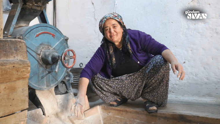 Bir kadın, değirmenin önünde oturarak un öğütüyor.