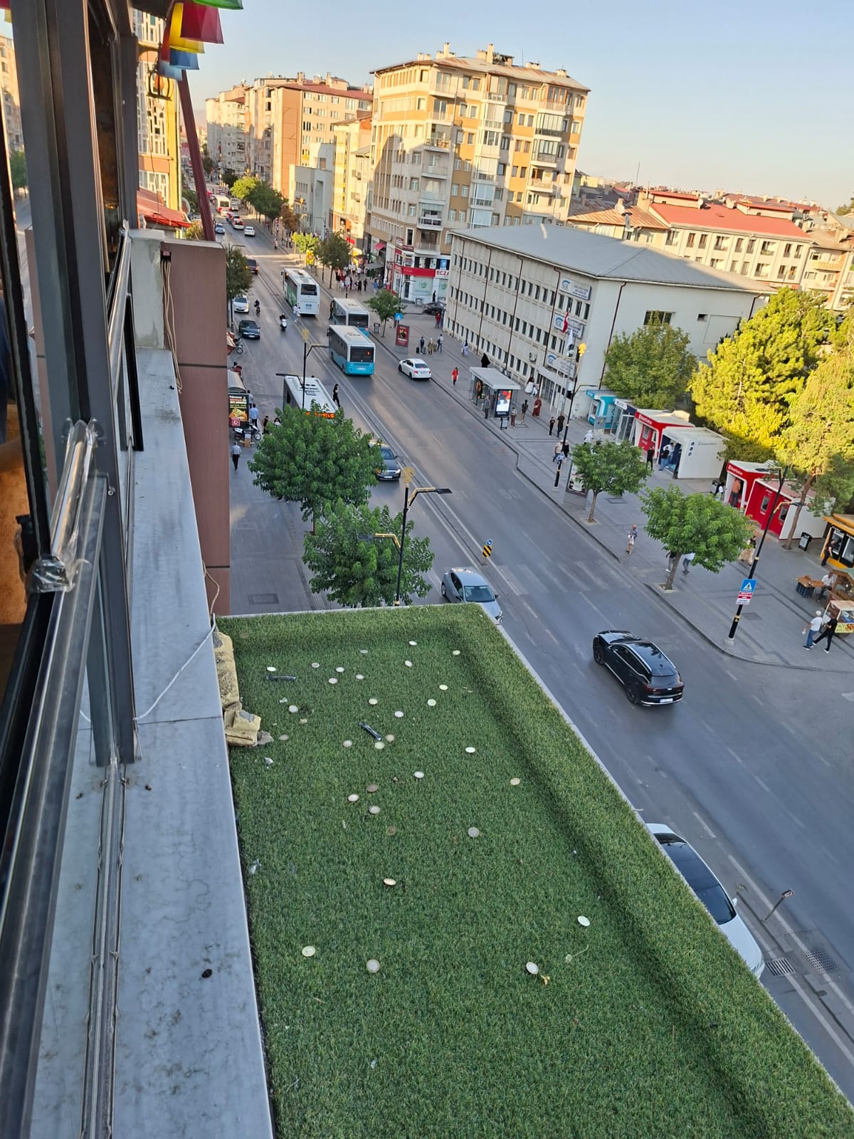 Kafenin balkonunda paralar yerleştirilmiş, aşağıda cadde ve araçlar görünmekte.