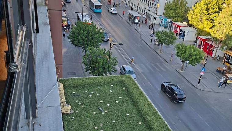 Kafenin balkonunda paralar yerleştirilmiş, aşağıda cadde ve araçlar görünmekte.
