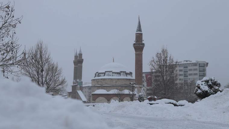 Karla kaplı alanda, kubbeli ve iki minareli cami ile çevresindeki ağaçlar ve binalar görülüyor.