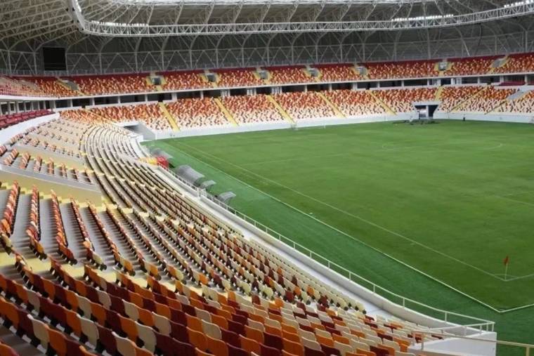 Boş tribünlerle çevrili yeşil futbol sahası ve üstü kapalı modern stadyumun iç görünümü.