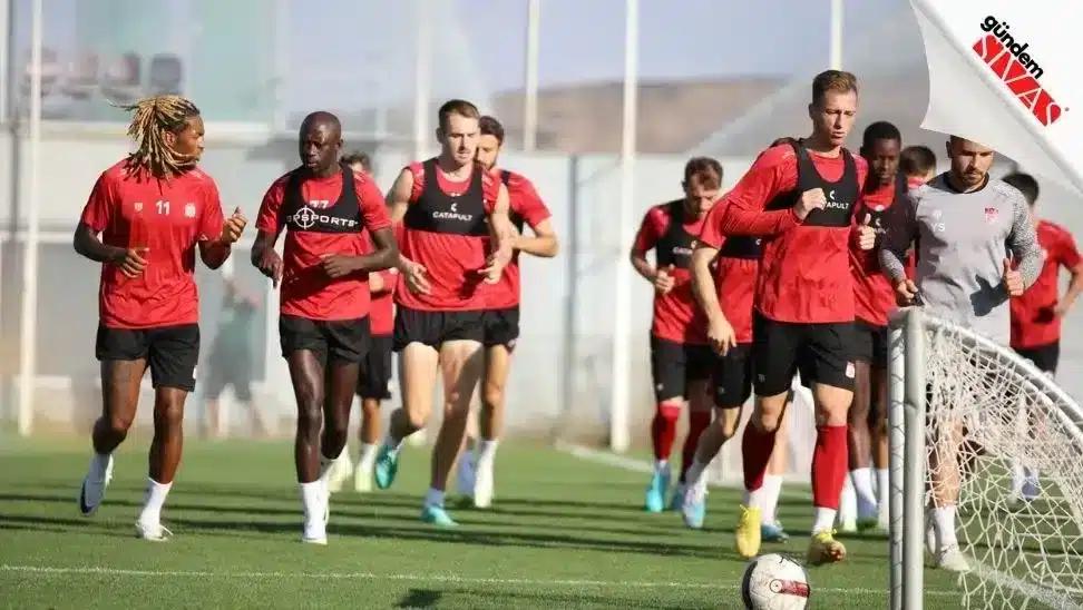 Antrenman yapan futbolcular, yeşil sahada koşu yapıyorlar.