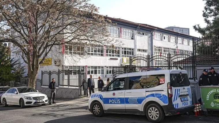 Demir çitlerle çevrili okul binası önünde bir polis aracı, park etmiş otomobil ve birkaç kişi görülüyor.