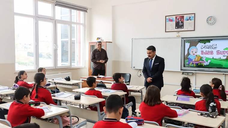 Sınıfta, kırmızı yelek giymiş öğrenciler öğretmenleriyle birlikte ders dinliyor.