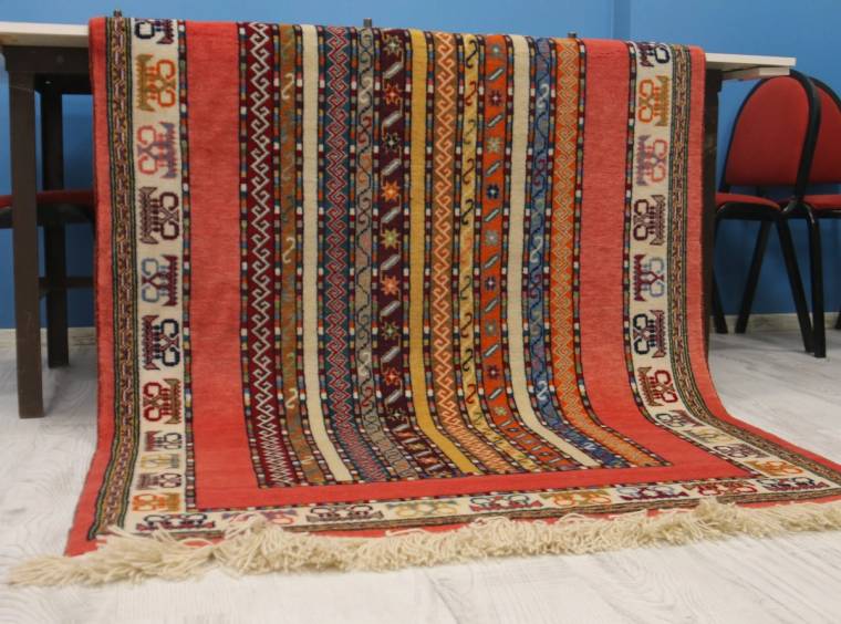 Sandalyelerin üzerine serilmiş, kırmızı ve çok renkli geometrik desenli el dokuması halı görülüyor.