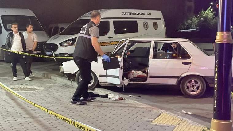 Geceleyin olay yeri inceleme araçlarının yanında, kapıları açık hasarlı beyaz otomobil ve yerde ekipman görülüyor.