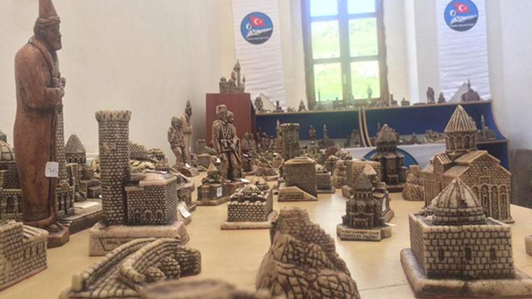 Masa üzerinde taş görünümlü çok sayıda biblo, heykel ve maket yapı sergileniyor.