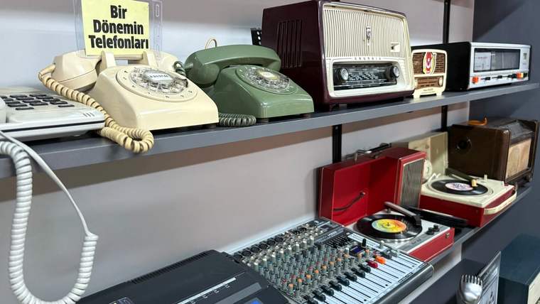 Raflarda eski telefonlar, radyolar, pikaplar ve ses mikseri sergileniyor; üstte “Bir Dönemin Telefonları” yazısı görülüyor.