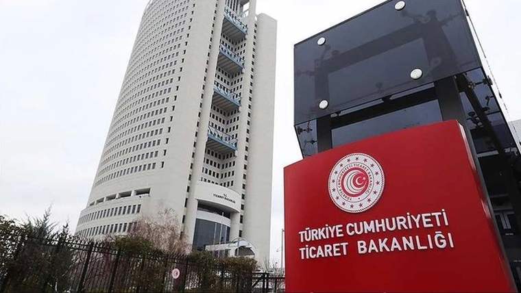 Üzerinde Türkiye Cumhuriyeti Ticaret Bakanlığı yazan kırmızı tabela, yüksek bir binanın önünde duruyor.