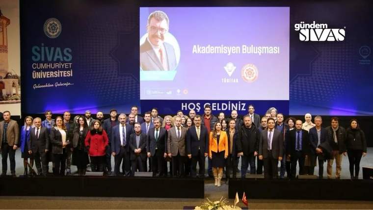Sivas Cumhuriyet Üniversitesi'nde bir grup insan, sahnede topluca poz veriyor.