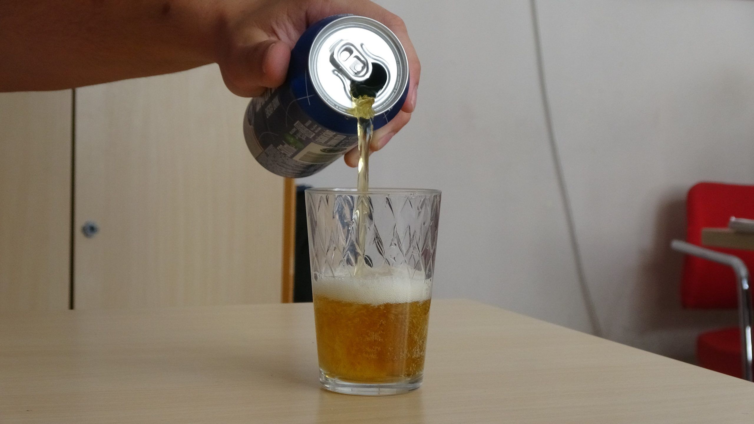 Bir el, bir kutu içeceği bir bardağa döküyor; bardakta köpüklü sarı bir sıvı var.