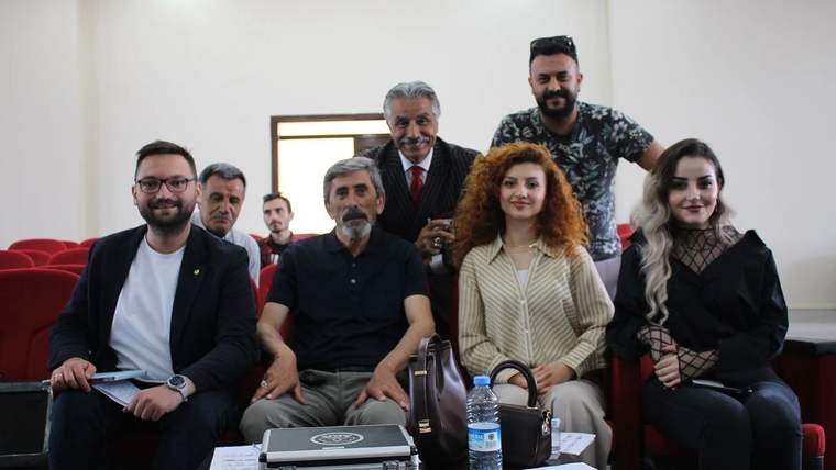 İç mekânda bir koltukta oturan dört kişi ve arkalarında duran üç kişi birlikte görüntüleniyor.