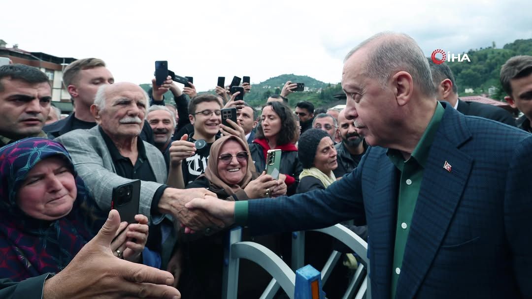 Önde bir kişi, bariyerin arkasındaki kalabalıkla el sıkışırken çevredekiler cep telefonlarıyla görüntü alıyor.