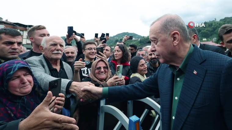 Önde bir kişi, bariyerin arkasındaki kalabalıkla el sıkışırken çevredekiler cep telefonlarıyla görüntü alıyor.