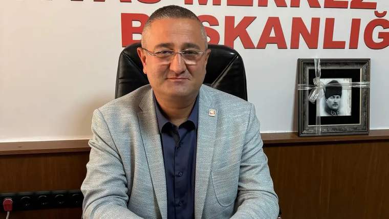 Bir kişi, ofisinde otururken gülümsemekte, arkasında Atatürk'ün bir fotoğrafı var.
