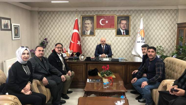 Bir ofiste, masa çevresinde oturan ve ayakta duran sekiz kişi; Türk bayrağı, parti bayrağı ve portreler görülüyor.