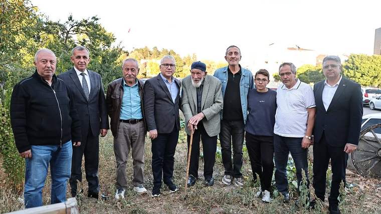Açık alanda, aralarında baston kullanan yaşlı bir erkeğin bulunduğu dokuz kişi yan yana duruyor.