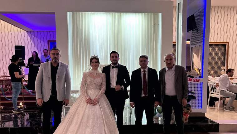 Düğün salonunda gelinlikli bir kadın, damat ve üç erkek birlikte yan yana poz veriyor.