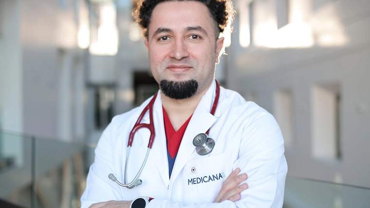 Beyaz lab coat giymiş bir doktor, gülümseyerek poz veriyor.