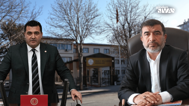 Bir kişi kürsüde konuşuyor, yanında başka bir kişi oturuyor; arka planda okul binası görünmekte.