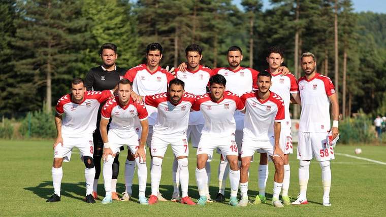 Sivasspor futbol takımı, antrenman sahasında poz veriyor. Takım oyuncuları beyaz formalar giymekte.