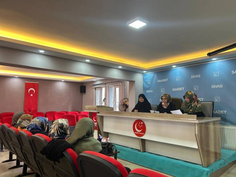 Saadet ve Sivas yazılı panonun önünde üç kadın masada otururken salonda dinleyiciler görülüyor.