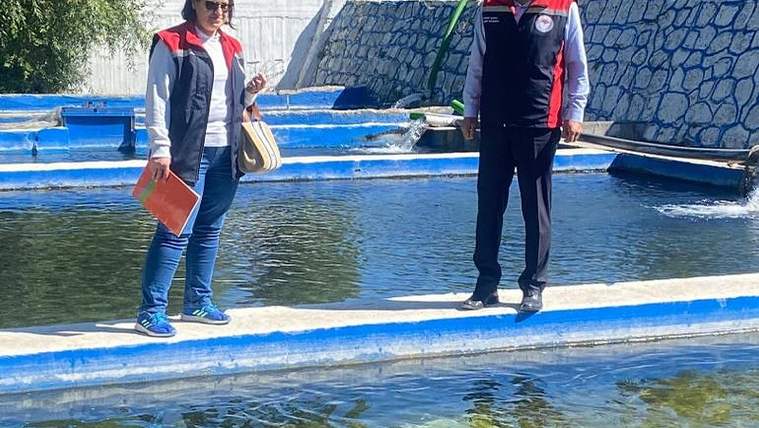 Açık havadaki su ürünleri tesisinde, beton havuzların yanında iki kişi ve bir balık ağı görülüyor.