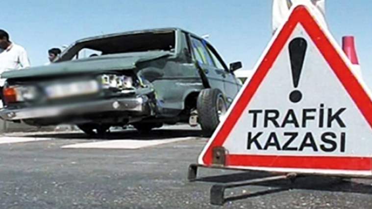 Hasar görmüş bir otomobilin yanında, üzerinde ünlem işareti ve “TRAFİK KAZASI” yazan uyarı levhası duruyor.